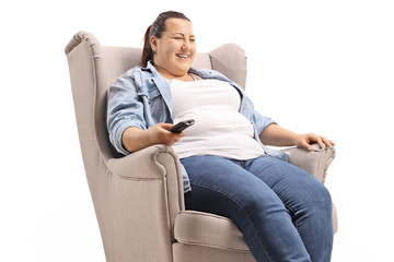 Wall Mural - Corpulent woman seated in an armchair watching television and smiling