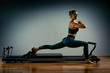 © Georgii - Young girl doing pilates exercises with a reformer bed. Beautiful slim fitness trainer on reformer gray background, low key, art light. Fitness concept