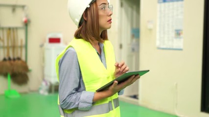 Poster - Asian  engineer wearing a Yellow safety helmet.while working with a Tablet for Machine inspection in the factory , the expression is serious face.