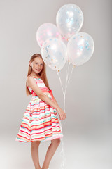 Wall Mural - Inclusive Beauty. Girl with freckles in dress standing isolated on grey holding balloons posing smiling joyful