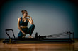 © Georgii - Young girl doing pilates exercises with a reformer bed. Beautiful slim fitness trainer on reformer gray background, low key, art light. Fitness concept