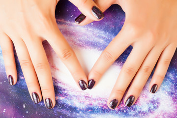 manicure stylish concept: woman fingers with nails purple glitter on nails like cosmos, universe background