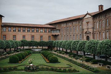 Hospital architecture of the Hotel Dieu in Toulouse France. Photography of an old medieval three-story european building from with a green plant garden in the courtyard.