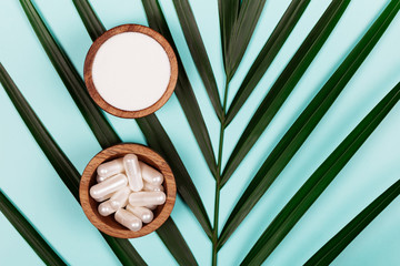 Wall Mural - Collagen in capsules and in powder in two wooden bowls on tropical leaf background