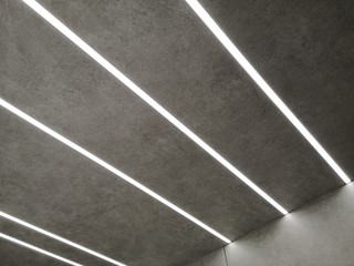 Poster - Glowing parallel lines of modern daylight lamps on ceiling or wall with texture resembling asphalt. Abstract minimal architecture, interior or technology background photo with geometric structure.