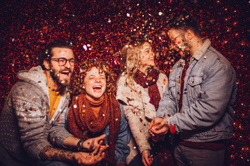 Group of beautiful young people throwing colorful confetti. New Year party