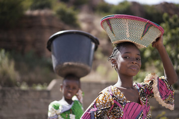 two proud african girls carrying heavy household items on their head