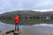 © Heike - Man with red jacket standing on typical canadian lake enjoying the nature and watching a yellow canoe. Having such a great time also while bad and cloudy weather
