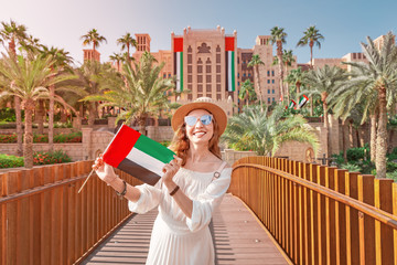 Wall Mural - happy girl holding UAE flag and admires beautiful view of the Madinat Hotel and Mall. Travel and vacation in Dubai and United Arab Emirates