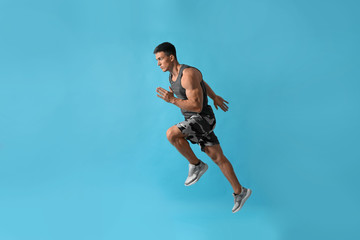 Canvas Print - Athletic young man running on light blue background, side view