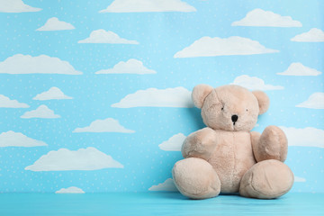 Wall Mural - Teddy bear on wooden table near wall with painted blue sky, space for text. Baby room interior