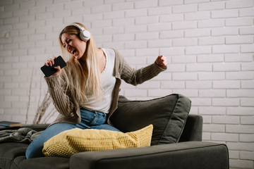 Beautiful woman dancing, singing and listening music on sofa