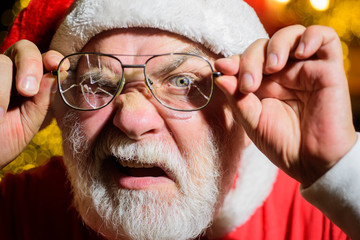 Wall Mural - Bearded man in Santa hat holds broken men's eyeglasses. Christmas. Santa man with broken glasses. Bearded Santa holds broken eye glasses. Santa Claus looking through cracked eyeglasses.