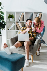 Wall Mural - attractive woman holding cup near injured man working from home with laptop