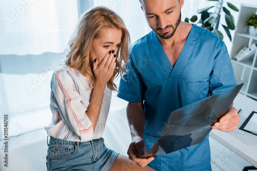 Fotomural handsome orthopedist and upset woman covering face while looking at x-ray