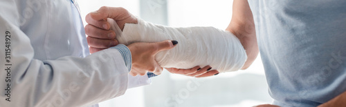 Fotografía panoramic shot of orthopedist touching injured hand of man