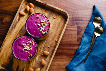 Top view of two glasses with violet berry smoothie are served crushed almond on a wooden tray.