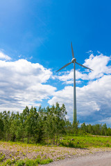 Single Wind Turbine in the middle of the green forest under blue sky with clouds. Windfarm, wind power plant