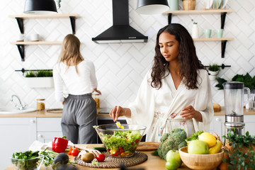 Two beautiful young girls on the white modern kitchen are making healthy breakfast