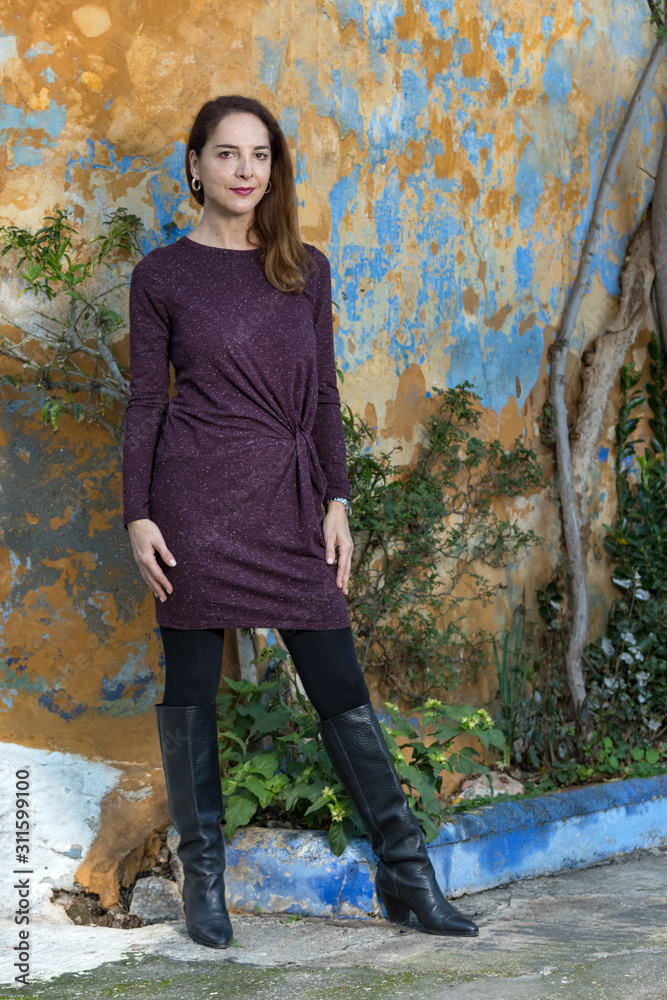 Full-length fashion portrait of a mature woman wearing high knee black boots  and a purple dress, standing, outdoors. Stock Photo | Adobe Stock