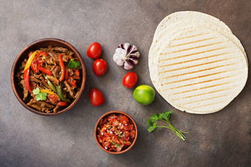 Wall Mural - Mexican dish fajitas meat with vegetables and salsa sauce on a dark rustic background. Flat lay, overhead.