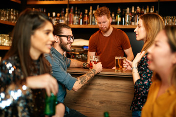 Wall Mural - Group of friends drinking beer, chatting and having good time at pub. Night out.