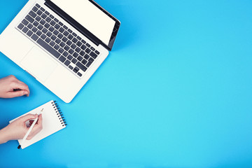 Poster - Woman working on laptop computer and notepad on blue background