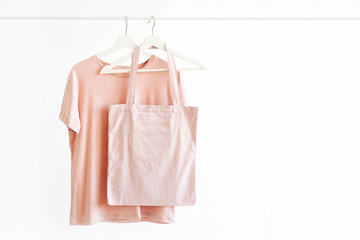 Wall Mural - T-Shirt in pastel pink color on hanger with eco bag on white background. Basic female clothes. Spring/summer outfit.
