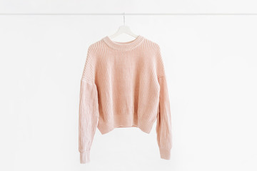 Wall Mural - Feminine pale pink warm sweater on hanger on white background. Elegant jumper fashion outfit. Spring wardrobe. Minimal concept.