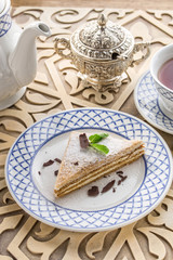 Wall Mural - Slice of layered honey cake with cup of tea on oriental wooden table