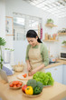 © makistock - Healthy food, diet concept. Asian woman cooking vegetable salad for dinner, cutting ripe tomatoes on wooden chopping board in kitchen at home.