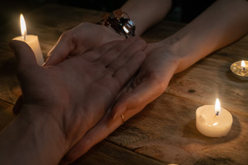 woman fortune-teller reads the lines of a man's hand and predicts his future, hands on a wooden background among candles. concept of magic, divination