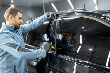 Car service worker sticking anti-gravel film on a window frame for protection at the detailing vehicle workshop. Concept of car body protection with special films