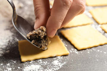 Woman making ravioli at grey table, closeup. Italian pasta