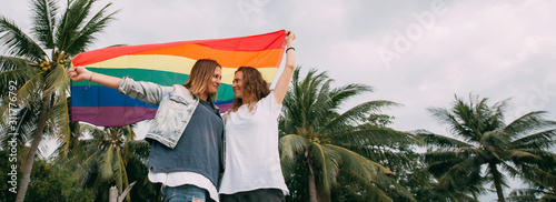 Fotografía Two women with rainbow flag on the beach on a background of palm trees