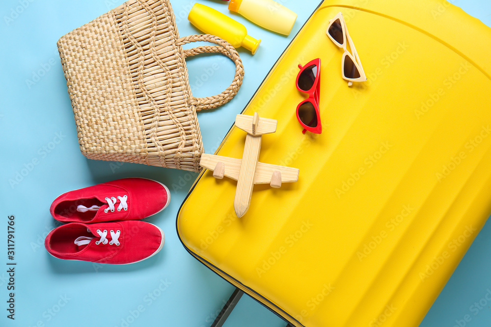 Suitcase with travel accessories on color background