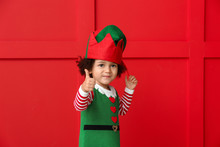 Little Girl In Costume Of Elf Showing Thumb-up Gesture On Color Background
