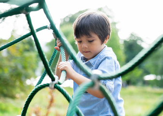 Soft focus of active kid climbing rope in the playground, High key light portrait Child enjoying activity in a climbing adventure park on summer sunny day, Cute little boy having fun on a playground.