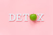 Body detoxification and healthy diet concept. Green natural fresh apple in word DETOX from white letters on pink background. Creative flat lay Top view Copy space