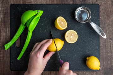 Wall Mural - Woman’s hands cutting a lemon on a black cutting board, green citrus squeezer, measuring cup