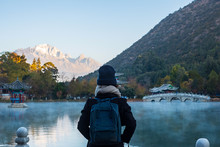 Young Woman Traveler Traveling At Black Dragon Pool With Jade Dragon Snow Mountain Background, Landmark And Popular Spot For Tourists Attractions Near Lijiang Old Town. Lijiang, Yunnan, China