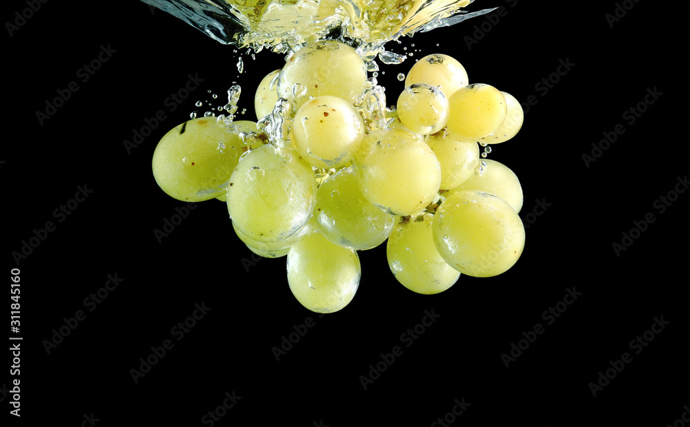 Green grape falling into water at black background