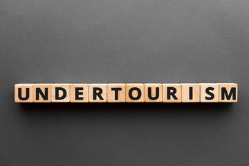 Undertourism - word from wooden blocks with letters, tourism marketing tactic less-frequented destinations undertourism concept, gray background