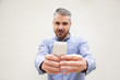 © Mangostar - Front view of focused man taking pictures on smartphone. Grey haired young man in blue casual shirt posing isolated over white background. Photo or phone photographer concept