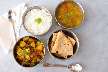 Wall Mural - Stainless steel Lunch Box or Tiffin with Indian food menu Chapati or Roti, Garlic Dal Tadka, White Rice and Potato or Jeera aloo. with spoons, tissue paper and glass of water. Copy space