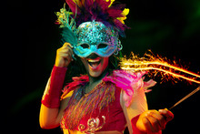 Beautiful Young Woman In Carnival Mask And Stylish Masquerade Costume With Feathers And Sparklers In Colorful Lights On Black Background. Christmas, New Year, Celebration. Festive Time, Dance, Party.