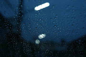 water rain drop on glass window with blur street light in night town background