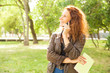 © Mangostar - Happy joyful woman with book talking on cell in park. Red curly haired young woman in casual posing outdoors. Communication outside concept