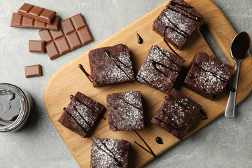 Wall Mural - Board with chocolate cake slices and chocolate on grey background, top view