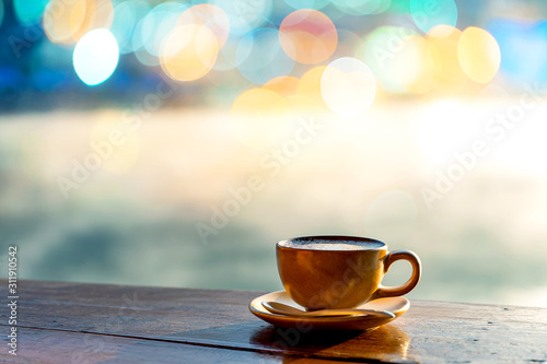 Fotografía Hot coffee cup on wooden table with warm sunlight and the misty at lake in morni